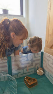 Twee kinderen bewonderen hun hamster die in de Omlet hamsterbox zit.