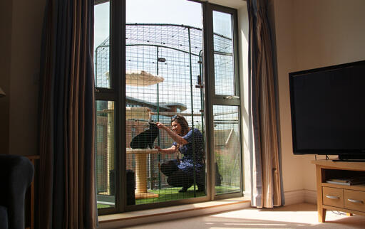 Een vrouw speelt met haar kat in een inloopren die op een balkon staat