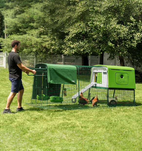 Man die het Eglu Cube verplaatsbaar kippenhok met wielen en handgrepen verplaatst